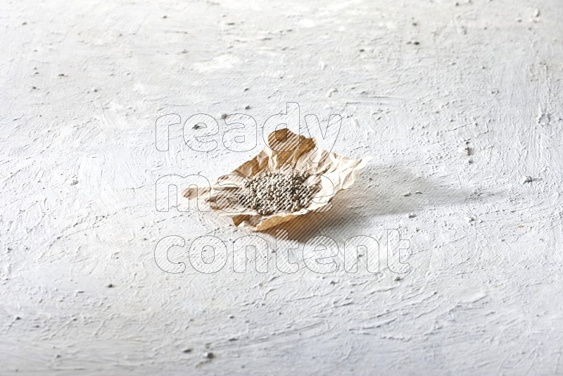 White pepper beads in a crumpled piece of paper on textured white flooring