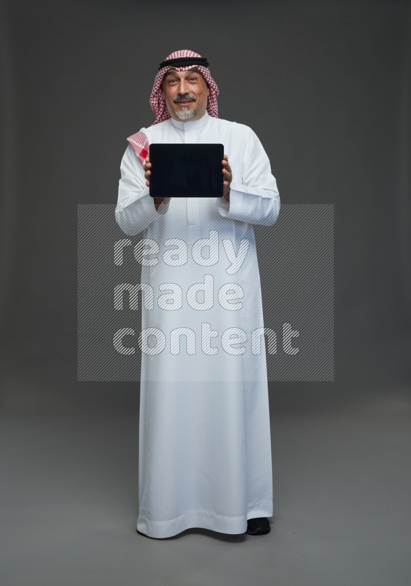 Saudi man with shomag Standing working on tablet on gray background