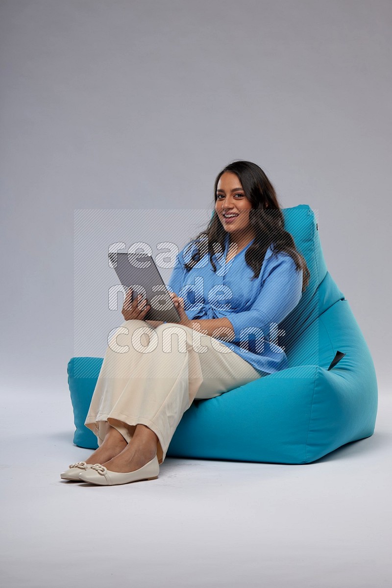 A woman sitting on a blue beanbag and working on tablet