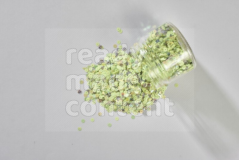 Colored flat sequins in a glass jar on grey background