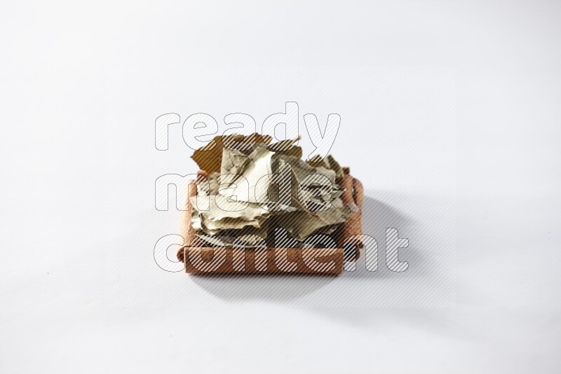 أربعة من أعواد القرفة مكونة شكل مربع بداخلها أوراق الغار علي خلفية بيضاء