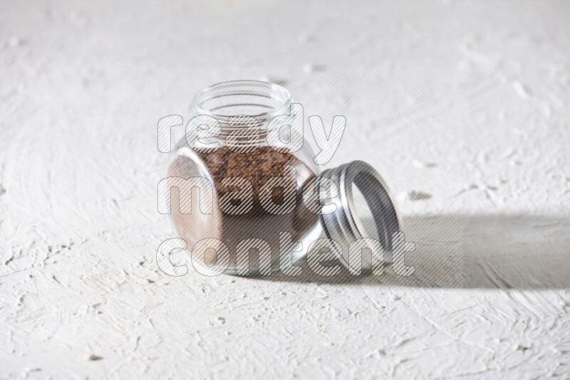A glass spice jar full of cloves powder on textured white flooring