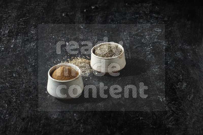 وعاءين بيج، أحدهما ممتلئ ببودرة الكمون والآخر ممتلئ بحبوب الكمون، على خلفية سوداء