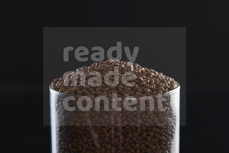 Brown lentils in a glass jar on black background