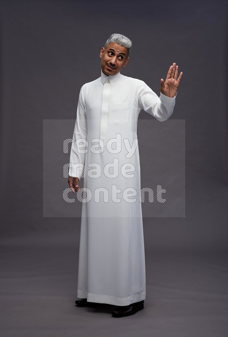 Saudi man wearing thob standing interacting with the camera on gray background