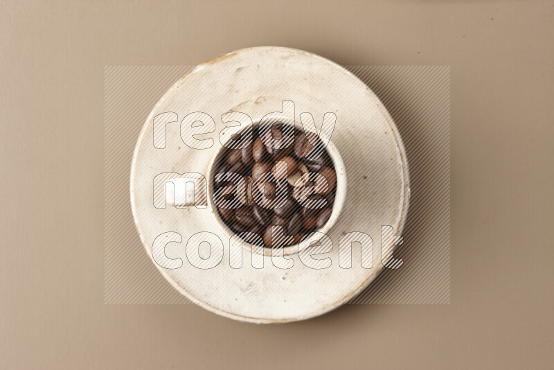 A beige pottery cup full of roasted coffee beans on beige background