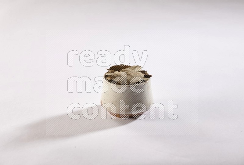 A beige pottery bowl full of dried bay leaves on white flooring