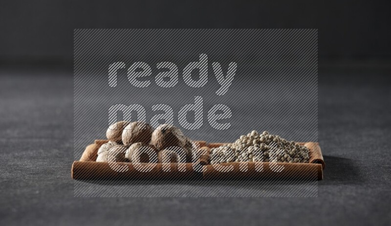 مربعان من أعواد القرفة ممتلئان بجوزة الطيب وحبوب الفلفل الأبيض علي خلفية سوداء