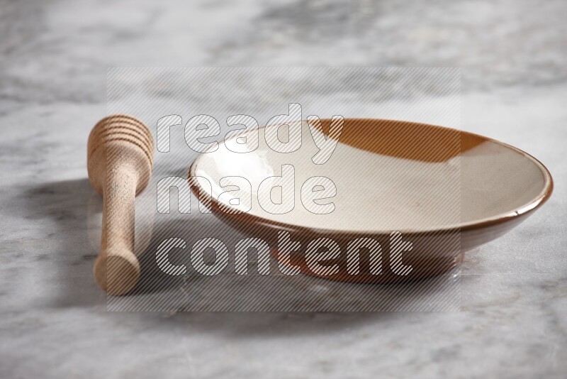 Multicolored pottery plate with wooden honey dipper on the side on grey marble background