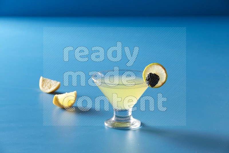 glass of lemon juice with lemon slice and berry on blue background
