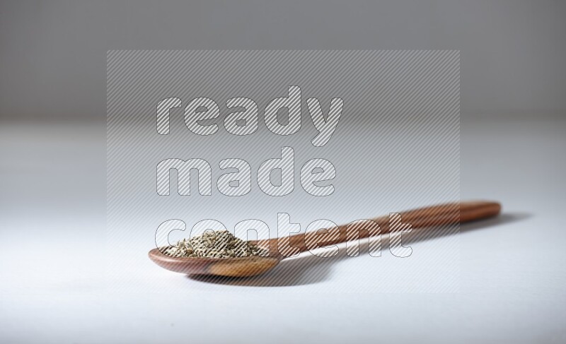 A wooden ladle full of cumin seeds on a white flooring
