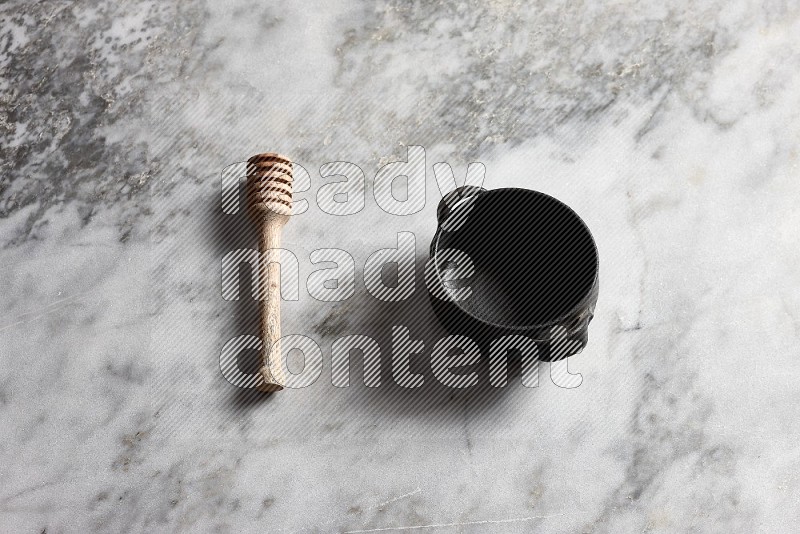 Black Pottery bowl with wooden honey handle on the side with grey marble flooring, 65 degree angle