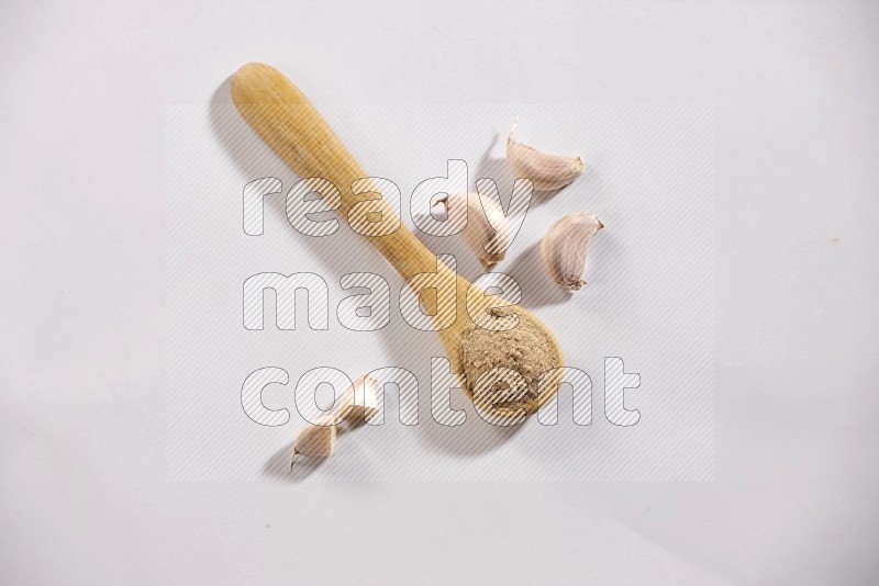 A wooden spoon full of garlic powder and garlic cloves beside it on a white flooring in different angles