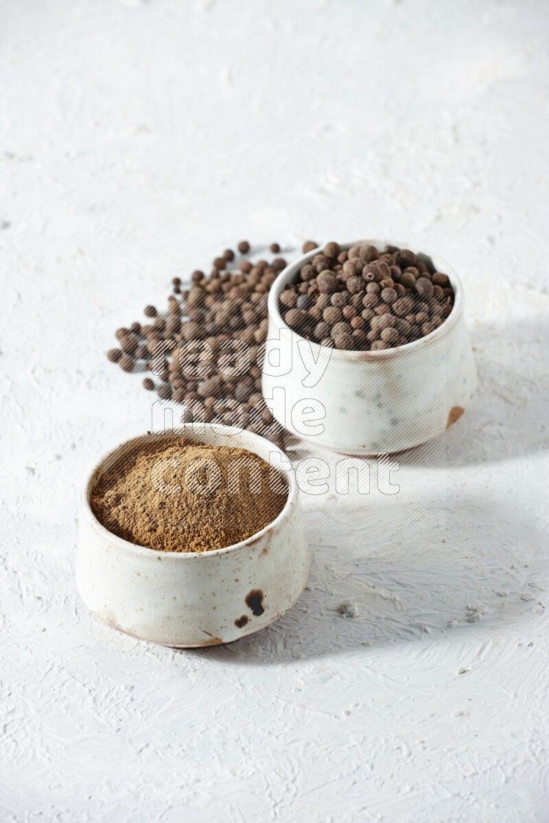 وعاءان بيج، أحدهما ممتلئ ببودرة بهار الفلفل الحلو والآخر بالحبوب مع البودرة والحبوب متناثرة على خلفية بيضاء