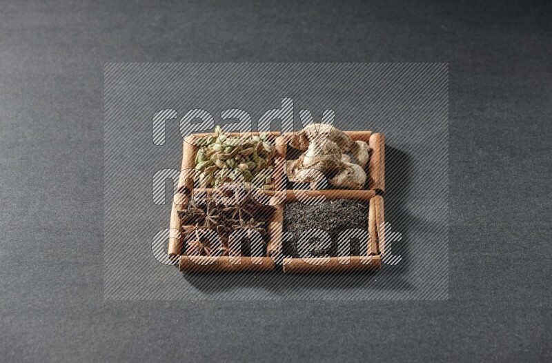 4 مربعات من عيدان القرفة ممتلئة بالشاي واليانسون النجمي والزنجبيل المجفف وحب الهيل على أرضية سوداء