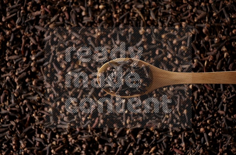 A wooden spoon full of cloves on cloves background and black flooring