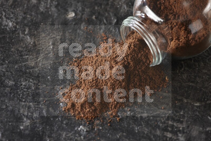 وعاء زجاجي للتوابل مقلوب ممتلئ ببودرة القرنفل والبودرة سقطت منه على أرضية سوداء