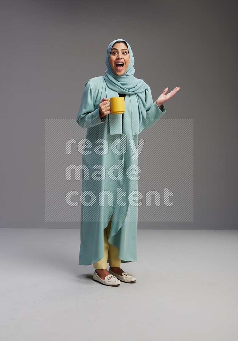Saudi Woman wearing Abaya standing  holding a mug on Gray background