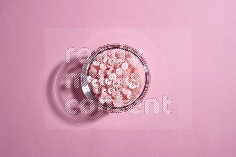 A glass bowl full of colored buttons on rose background