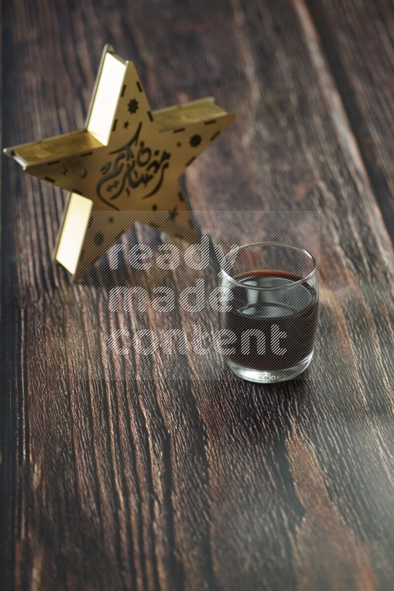 A wooden golden star lantern with different drinks, dates, nuts, prayer beads and quran on brown wooden background