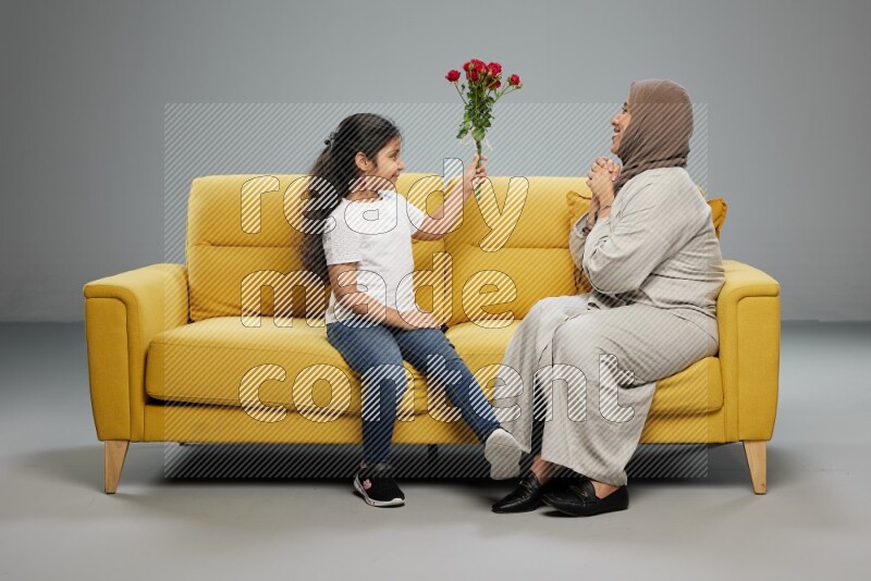 A girl sitting giving flowers to her mother on gray background