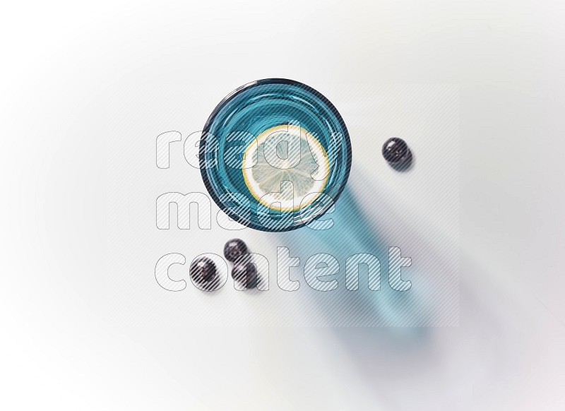 Blue transparent glass filled with blueberries decorated with lemon slices on a white background