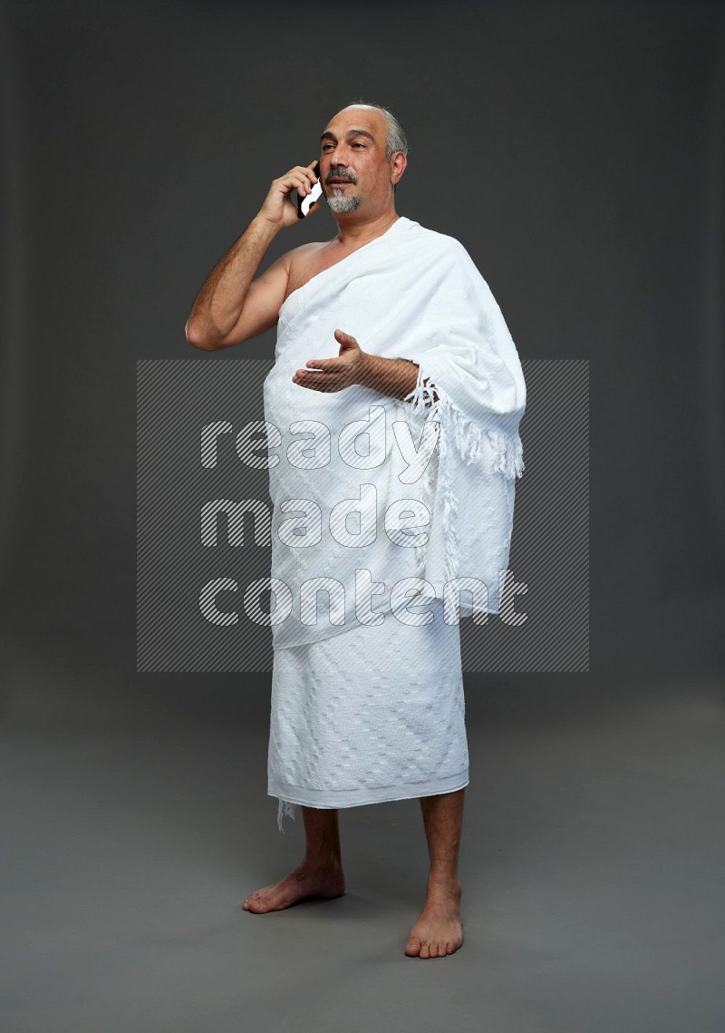 A man wearing Ehram Standing talking on phone on gray background