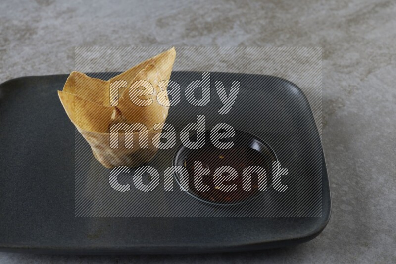 wonton cups with soy sauce ramkin on rectangle dark grey ceramic plate on grey textured counter top