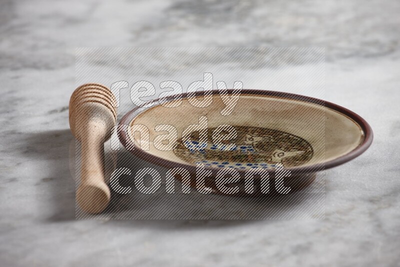 Decorative pottery plate with wooden honey dipper on the side on grey marble background