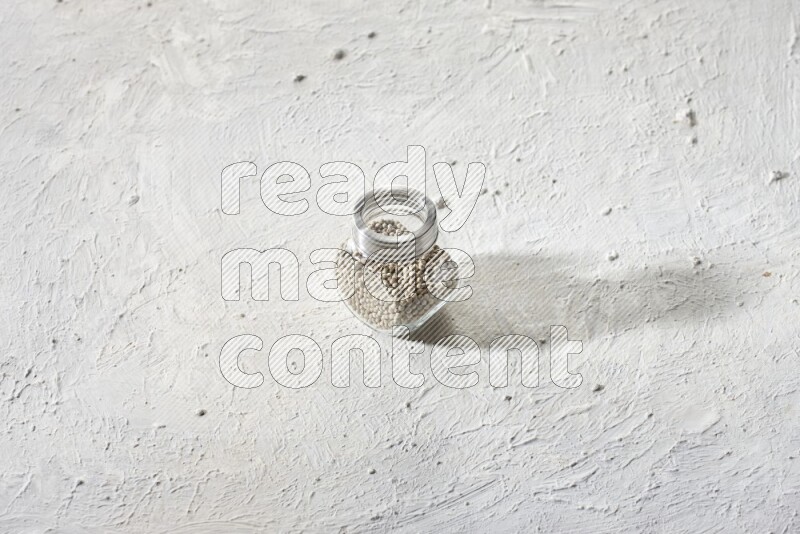 Herbal Glass jar full of white pepper beads on textured white flooring