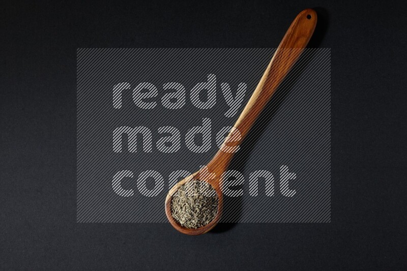 A wooden ladle full of cumin seeds on black flooring