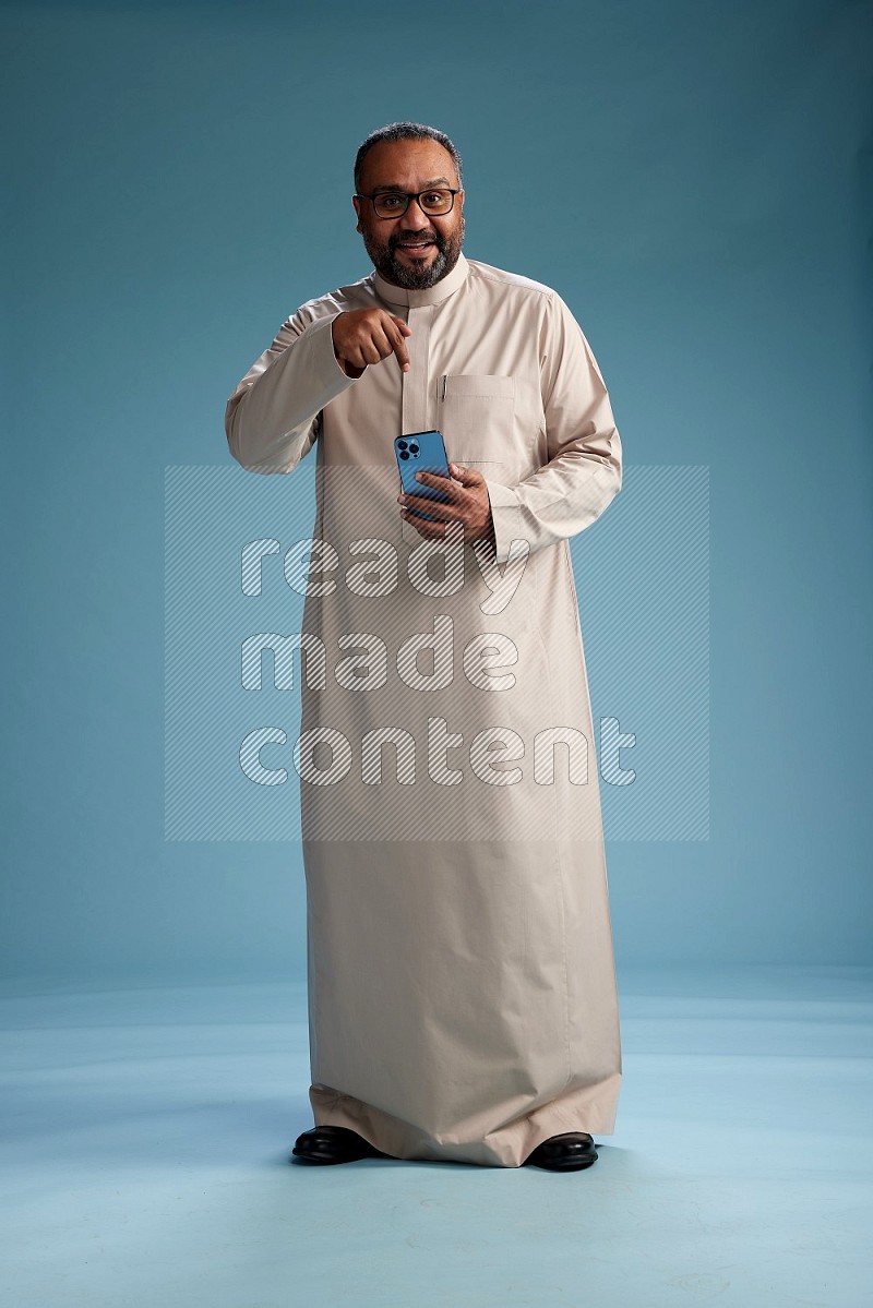 Saudi Man without shimag Standing texting on phone on blue background