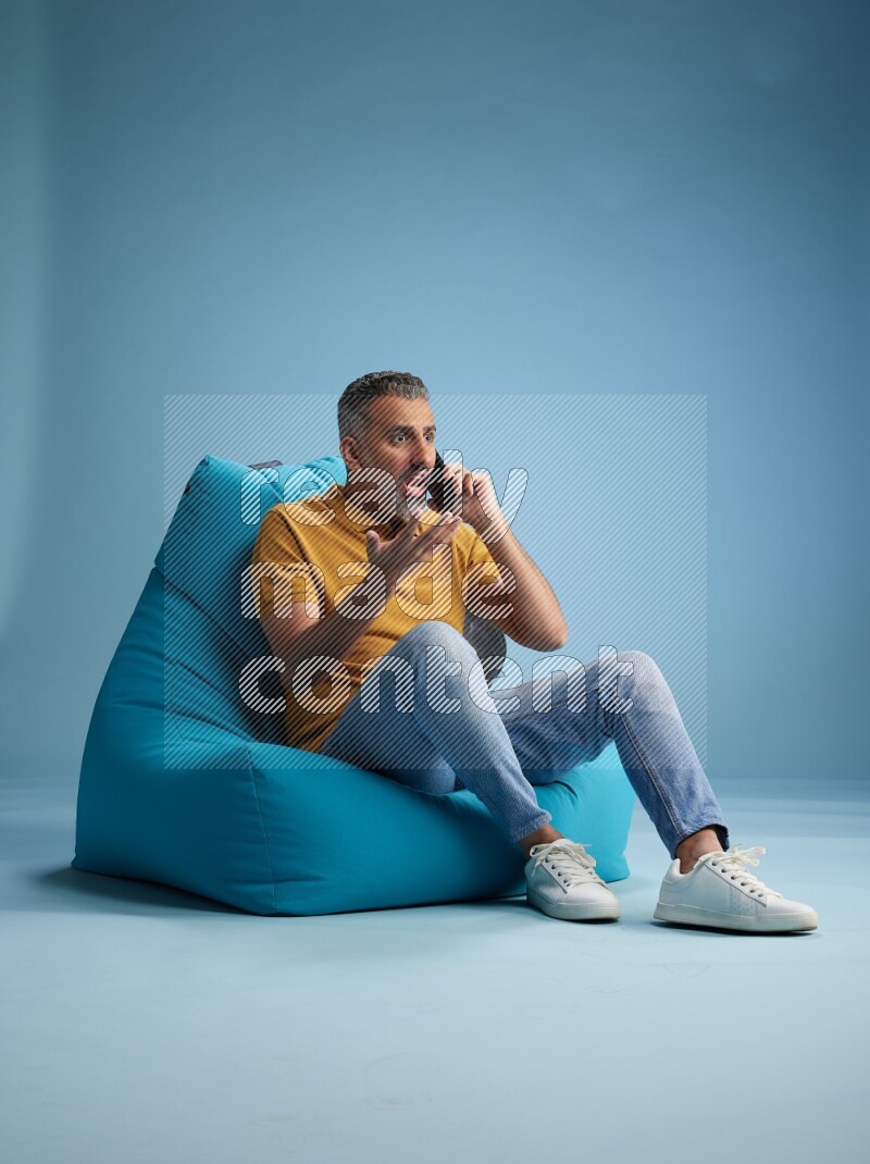 A man sitting on a blue beanbag and talking on the phone