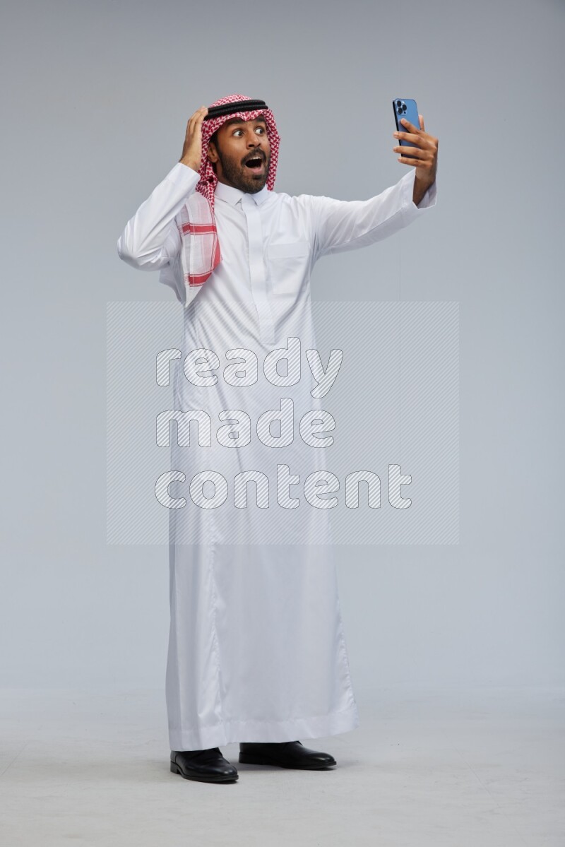 Saudi man Wearing Thob and shomag standing taking selfie on Gray background