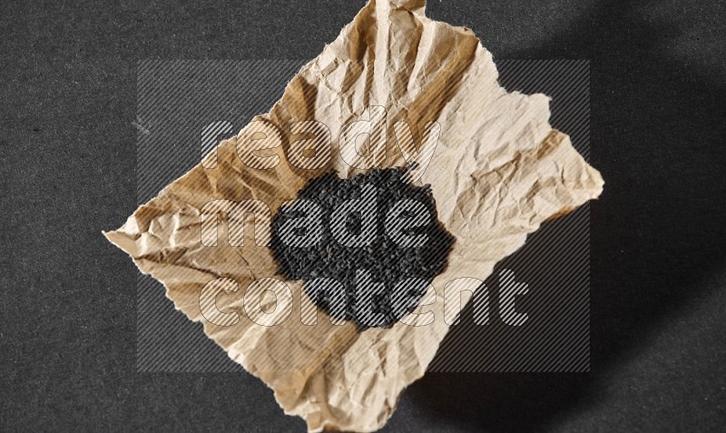 A crumpled piece of paper full of black seeds on a black flooring