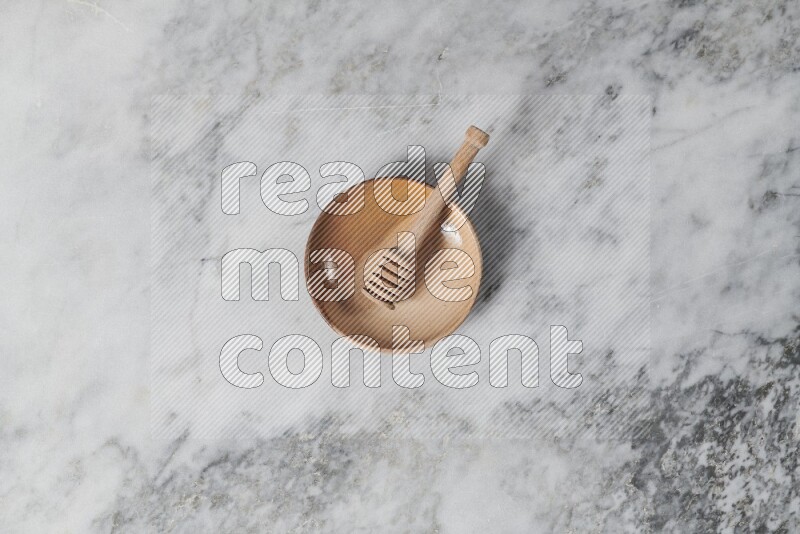Multicolored pottery plate with wooden honey dipper in it on grey marble background