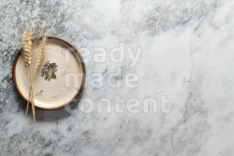 Wheat stalks on Decorative Pottery Plate on grey marble flooring, Top view