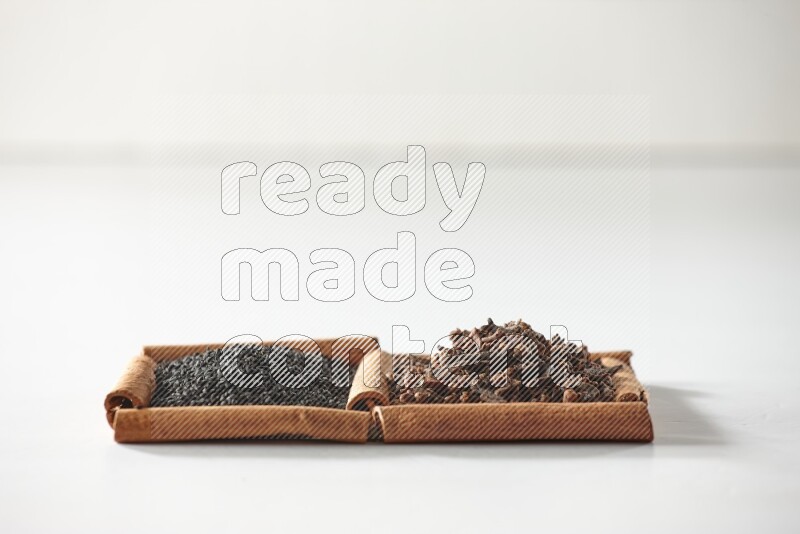 2 squares of cinnamon sticks full of cloves and black seeds on white flooring