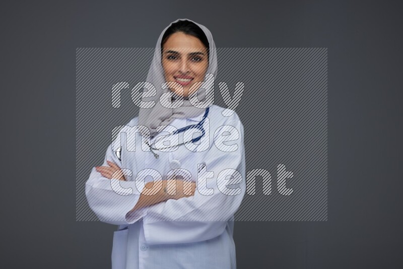 A female doctor wearing a light gray head scarf standing on grey background.
