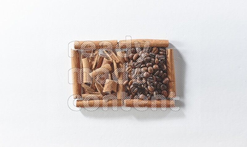 مربعان من أعواد القرفة ممتلئان بحبوب القهوة وقطع من القرفة علي خلفية بيضاء