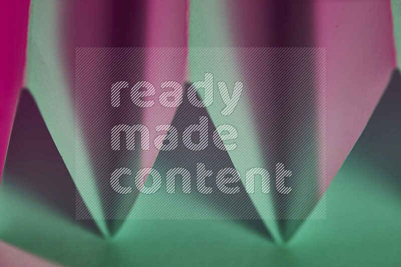 صورة مجردة مقربة تظهر طيات ورقية هندسية حادة بتدرجات اللون الأخضر والوردي
