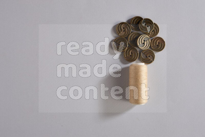 A beige sewing thread spool with colored buttons on grey background