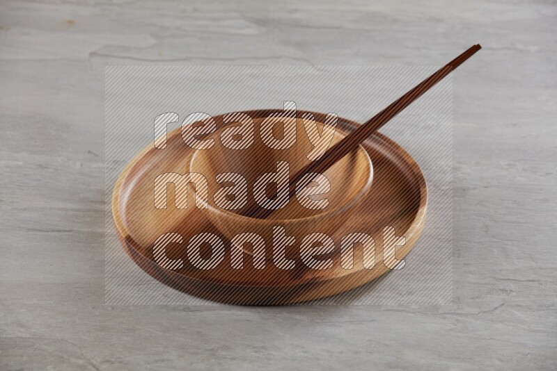brown wood round bowl on top of brown wood round plate and wood chopsticks, on grey textured countertop