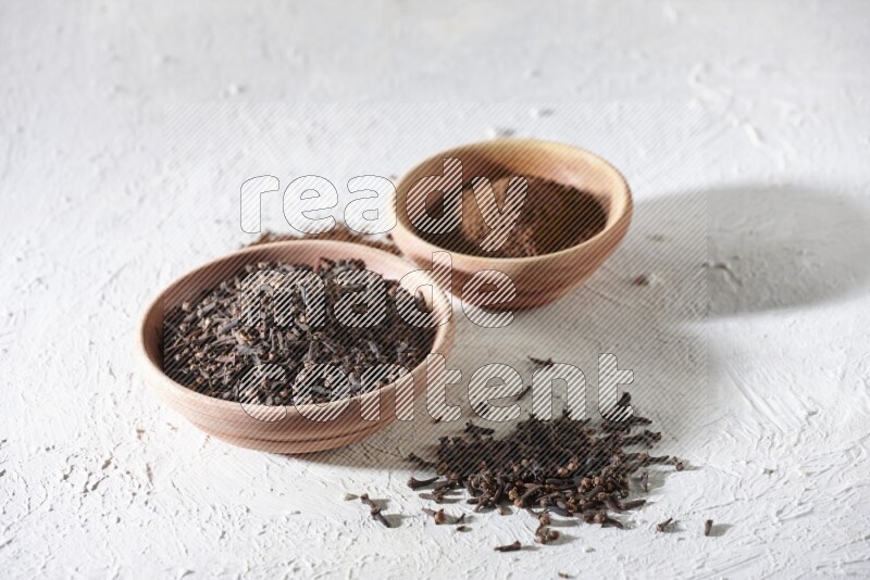 2 wooden bowls full of cloves powder and whole cloves on a textured white flooring