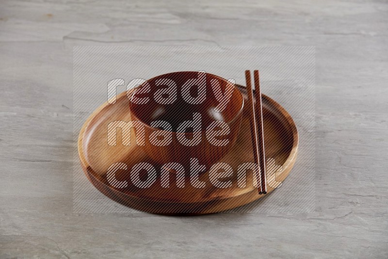 brown wood round bowl on top of brown wood round plate on grey textured countertop