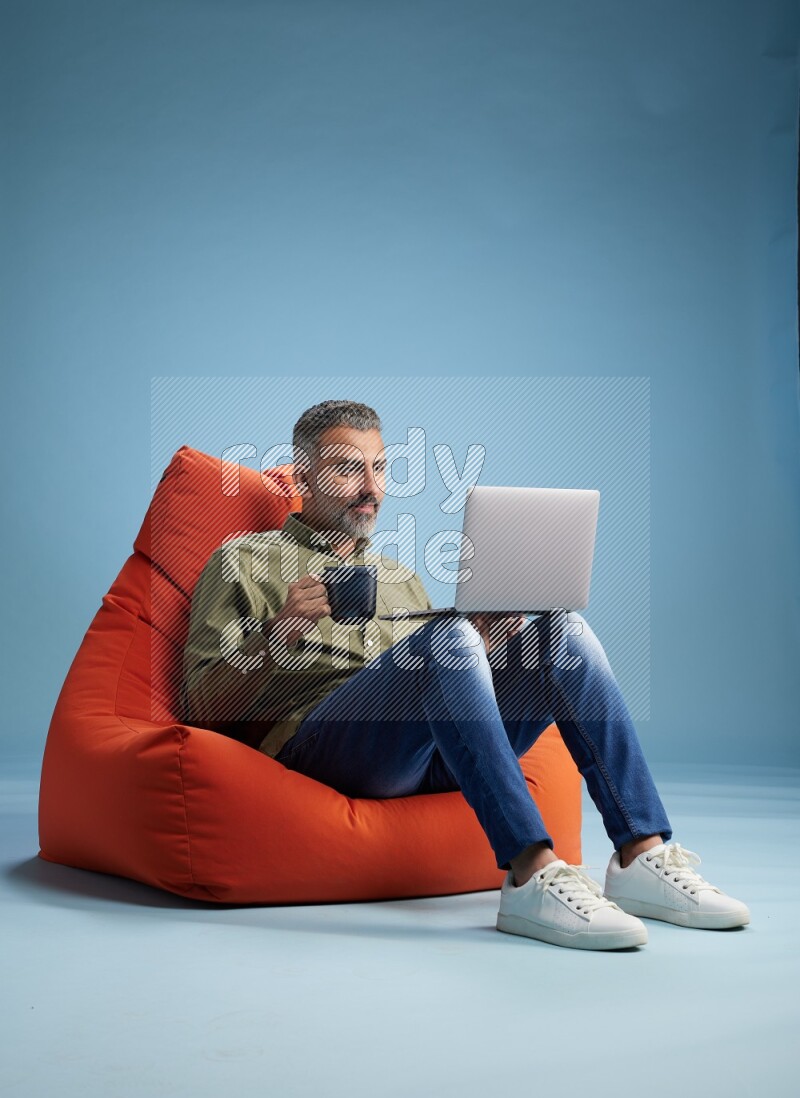 A man sitting on an orange beanbag and working on laptop