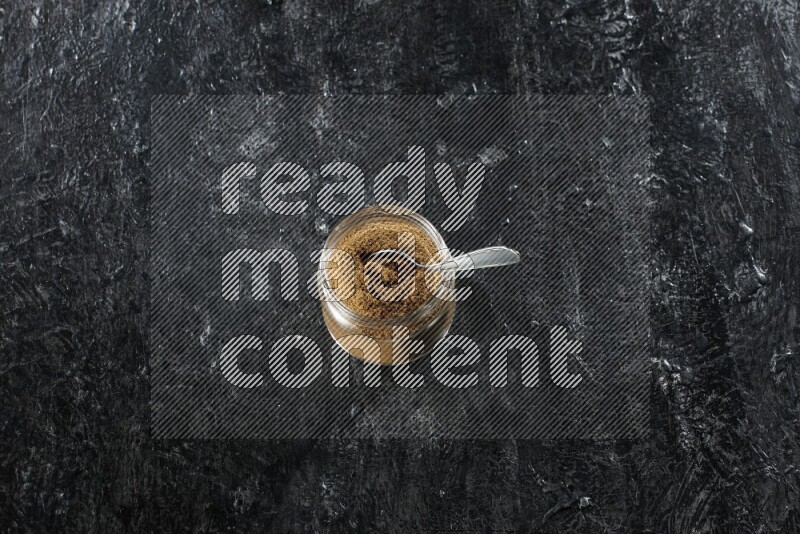 وعاء زجاجي للتوابل وملعقة معدنية ممتلئين ببودرة الكمون على خلفية سوداء