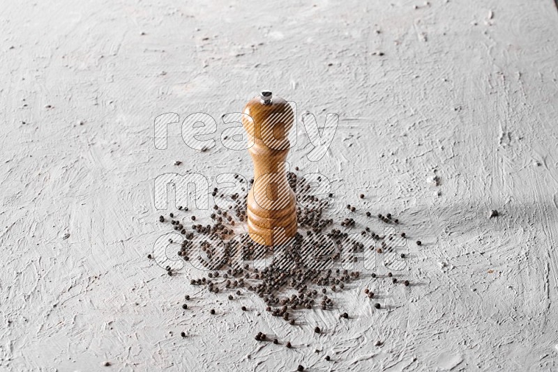 A wooden grinder with black pepper beads on a textured white flooring