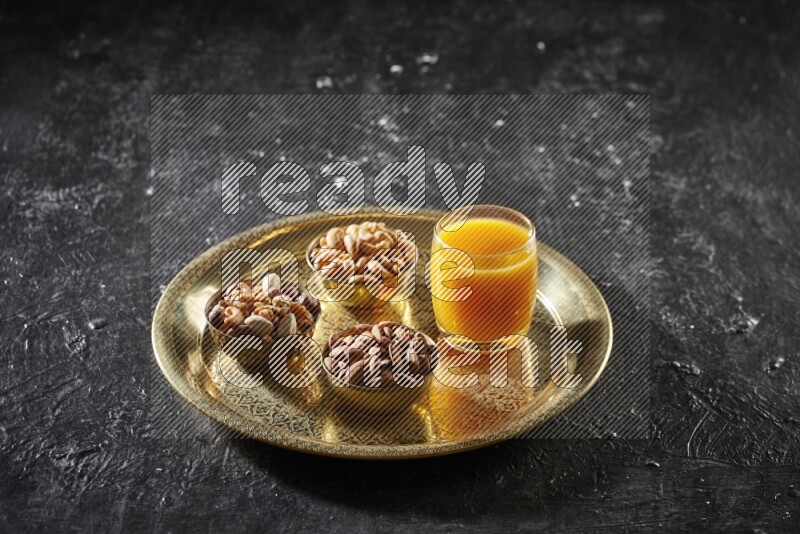 مكسرات في أطباق معدنية مع مشروب قمر الدين على صينية علي خلفية سوداء