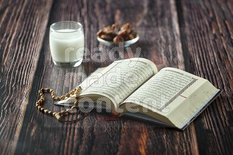 Quran with dates, prayer beads and different drinks all placed on wooden background